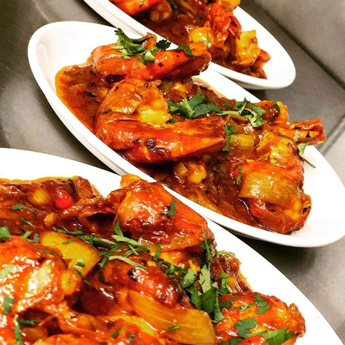Three white plates of large prawns in a rich red-orange sauce with onions and fresh green herbs.
